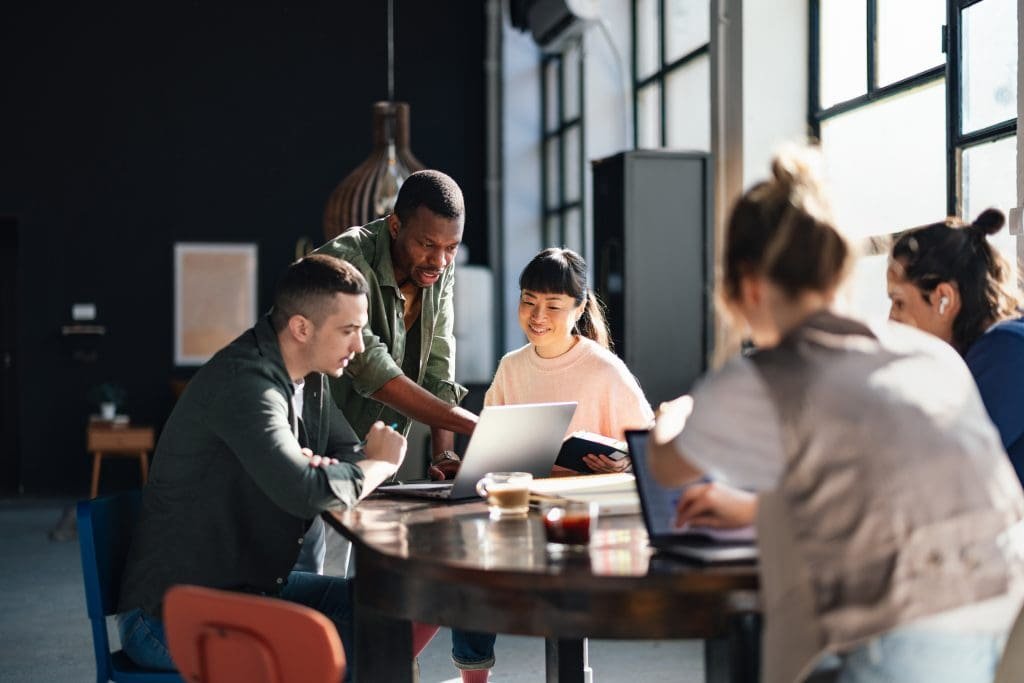 Group of professionals collaborating around a table with laptops and documents in a modern office space.